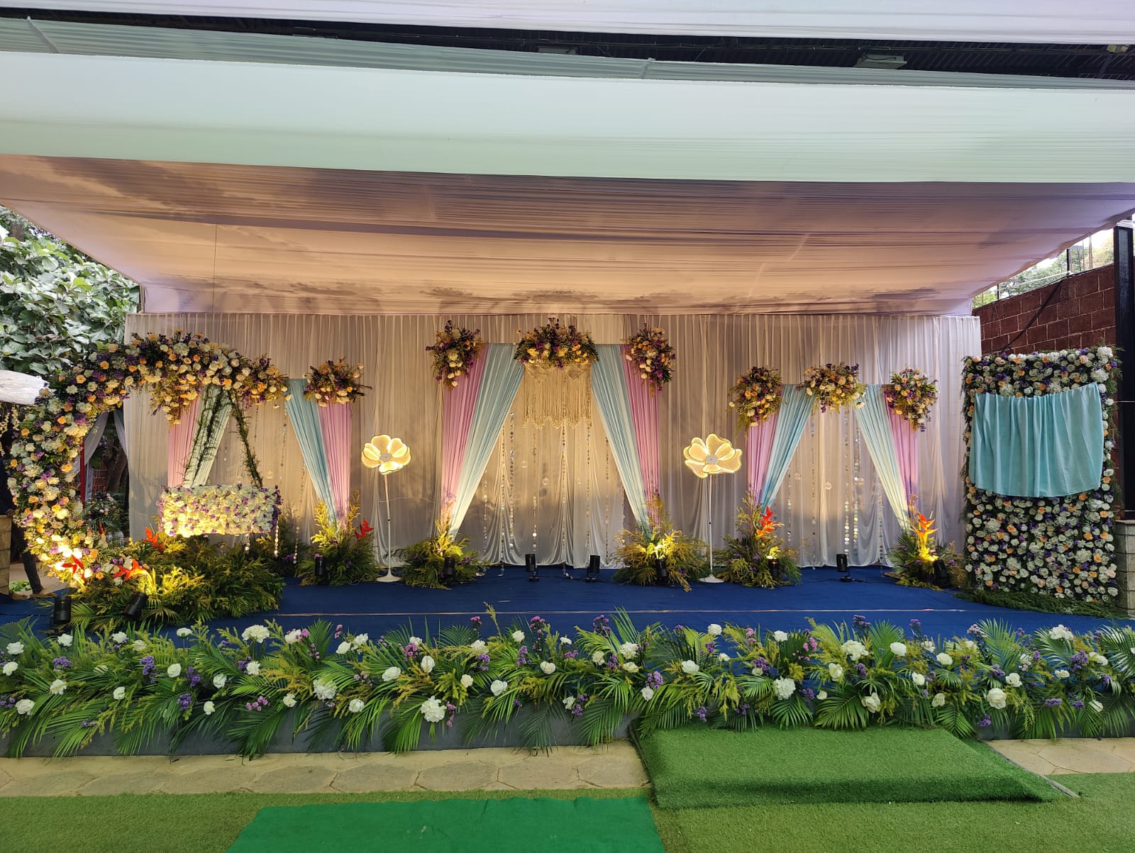 Open-air lawn mandap framed by floral garlands and ceremonial seating.
